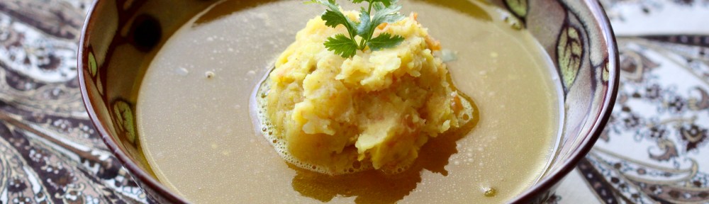 A bowl of soup with mash in the middle