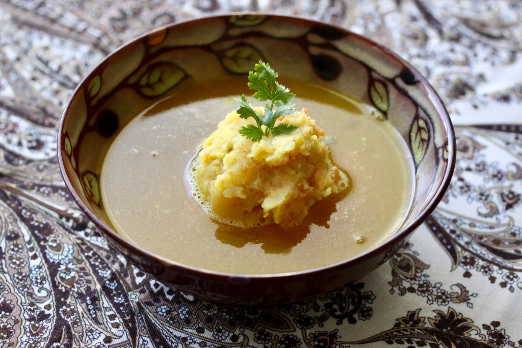 A bowl of soup with mash in the middle