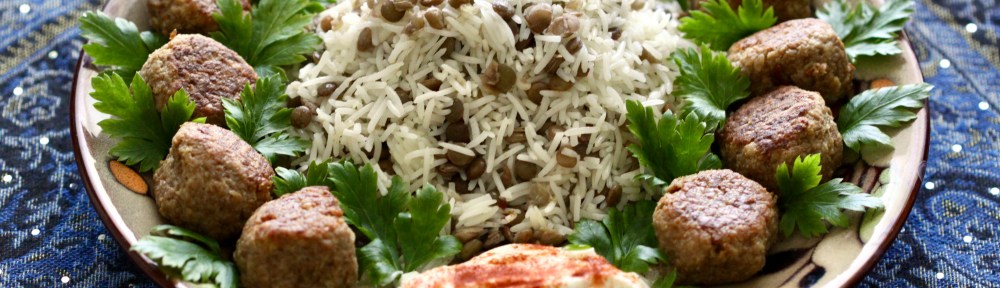 A plate of addas pilau and meatballs with parsley and paprika-adorned yogurt