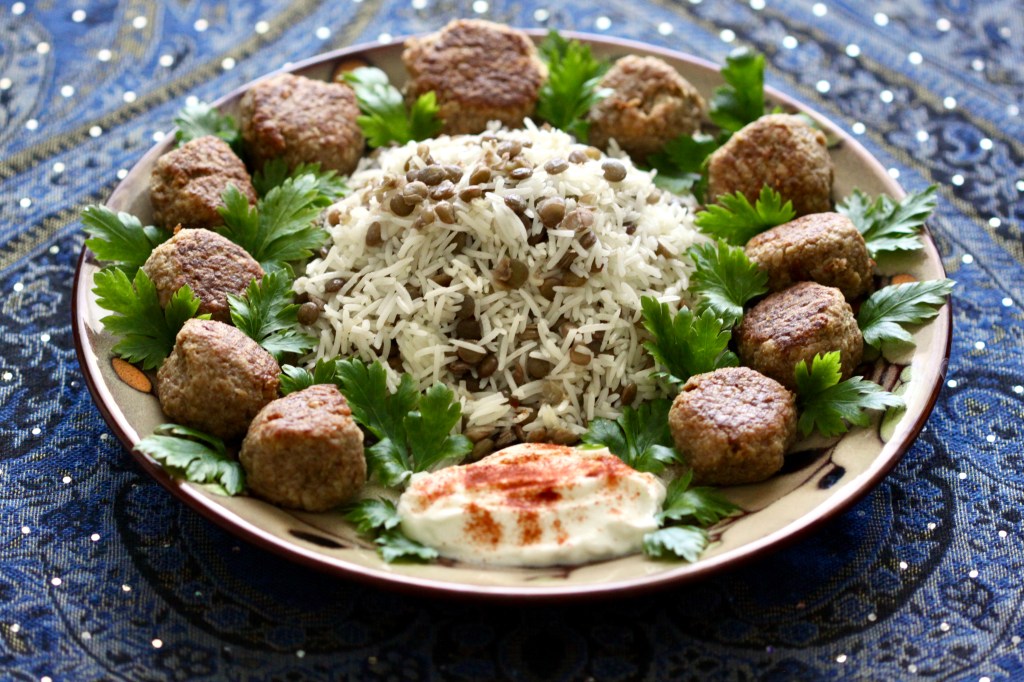A plate of addas pilau and meatballs with parsley and paprika-adorned yogurt
