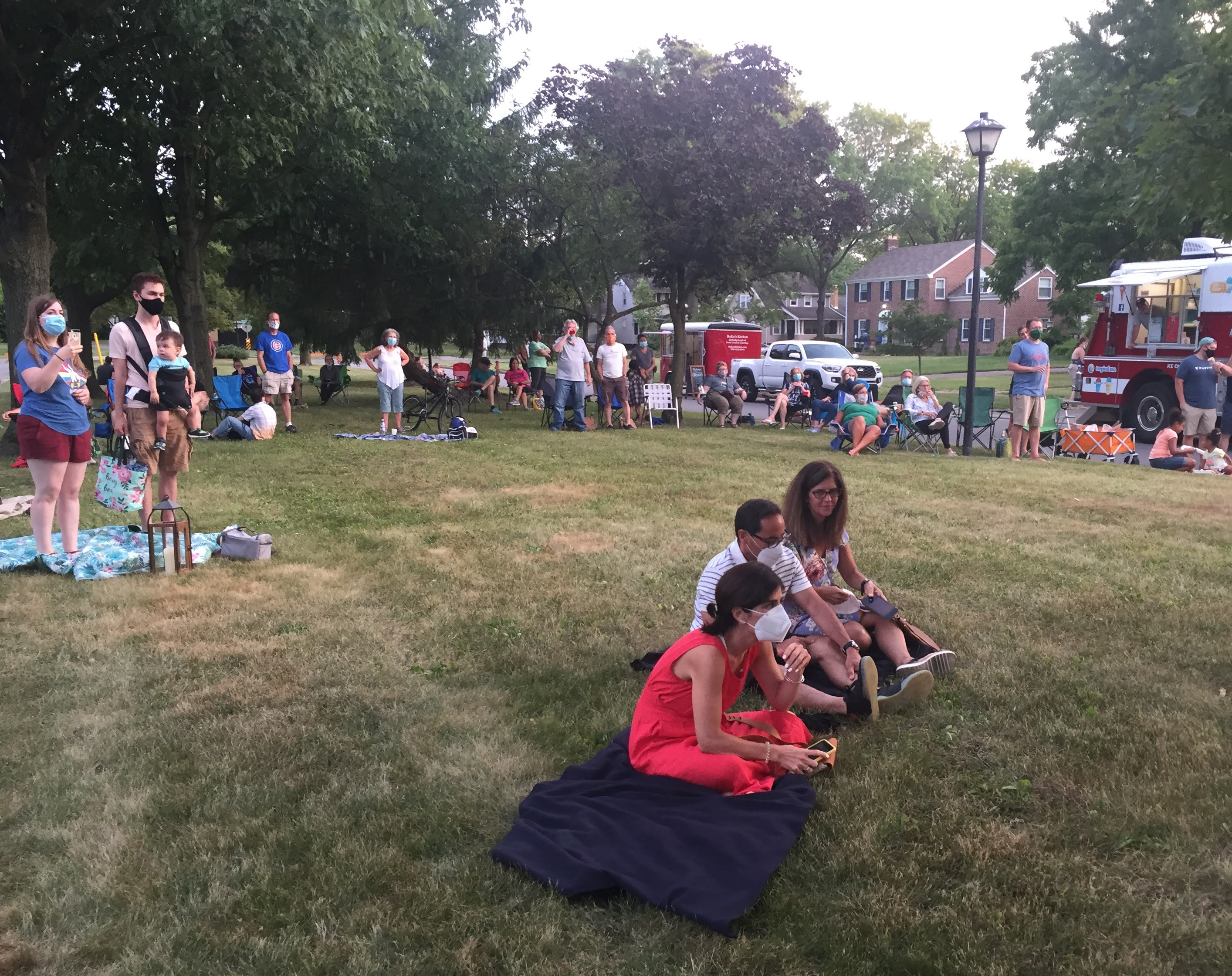 About twenty people stand and sit on a large lawn.