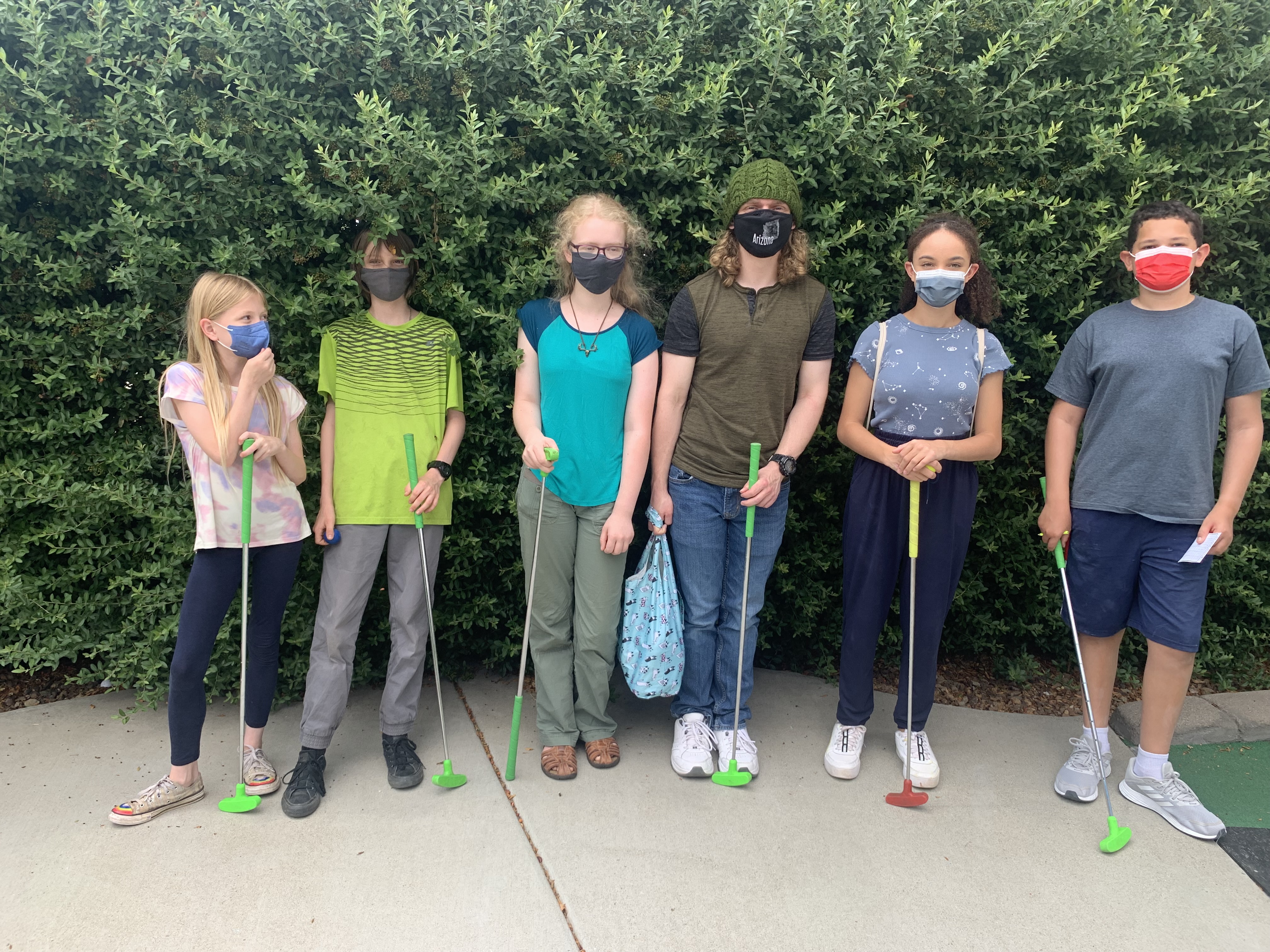 Six young people hold mini-golf clubs.