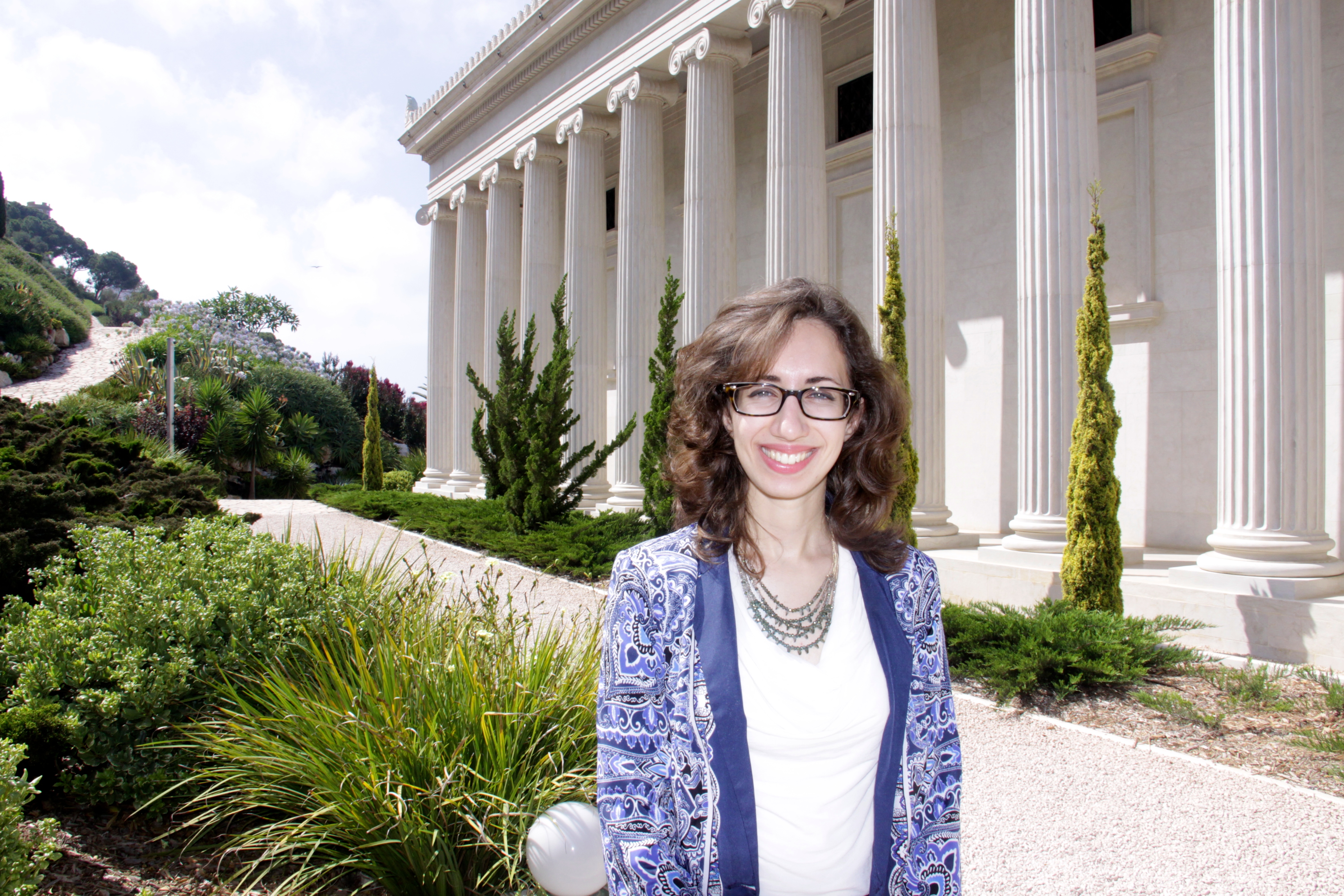 A young woman poses in front of a neoclassical building with a colonnade.