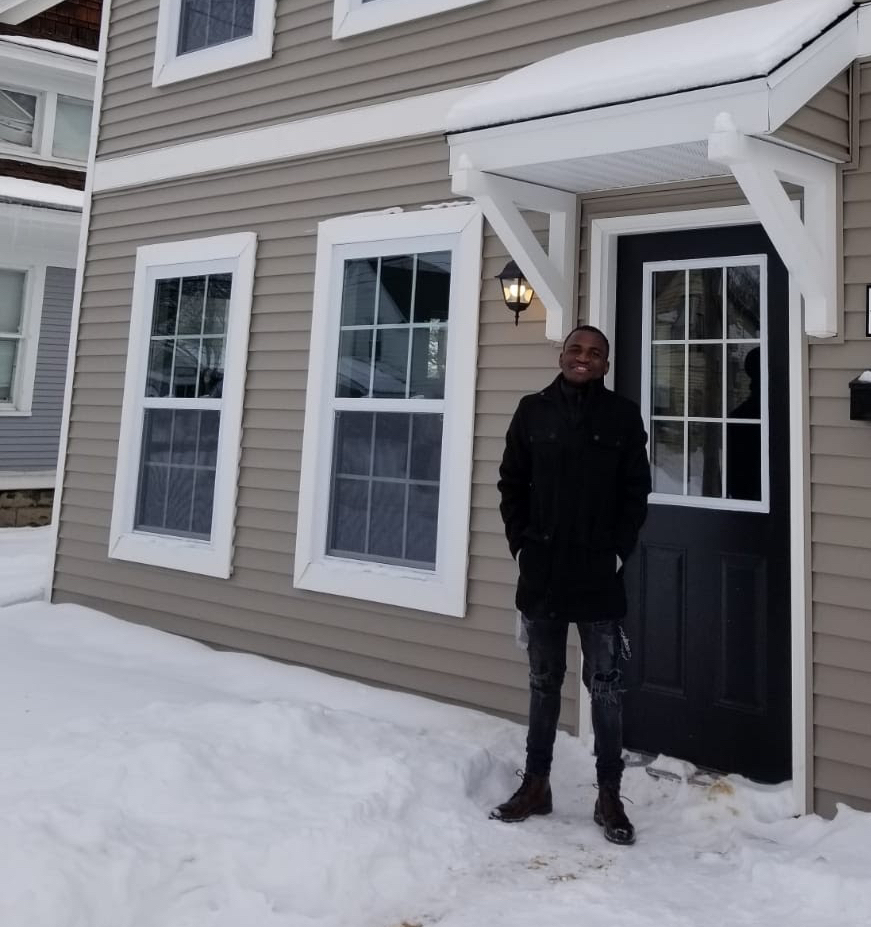 A young man stands in front of a snow-covered house.