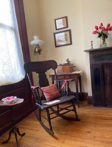 A rocking chair sits between a window and a fireplace.