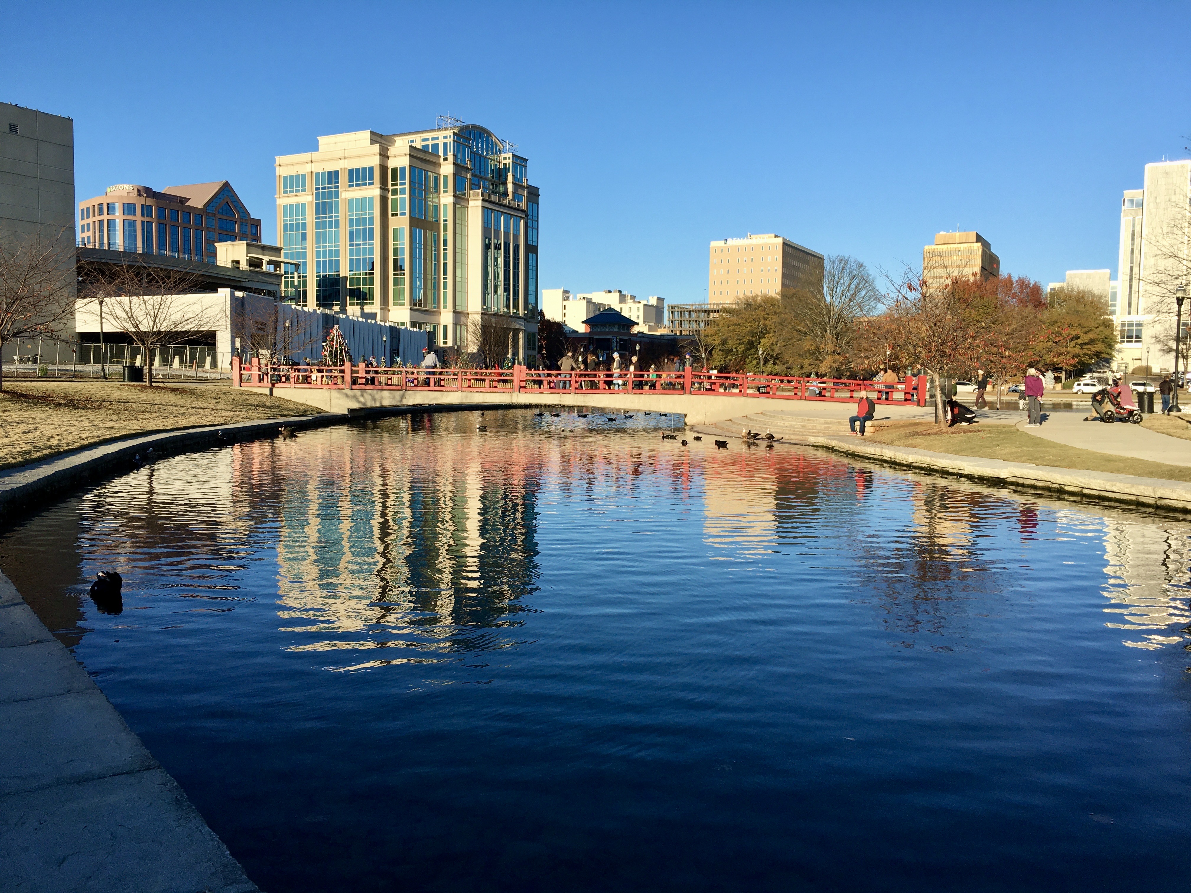 Modern buildings stand next to a canal. A footbridge spans the canal.