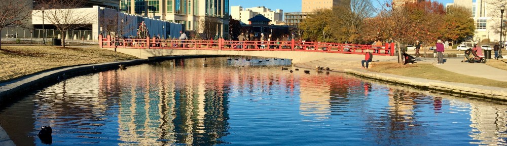Modern buildings stand next to a canal. A footbridge spans the canal.