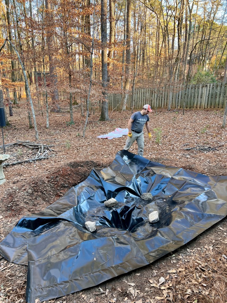 A man arranges a large, black sheet of plastic on the ground.