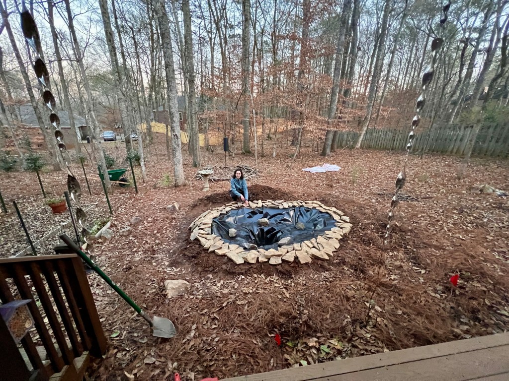 A woman sits next to the foundation of a small pond.