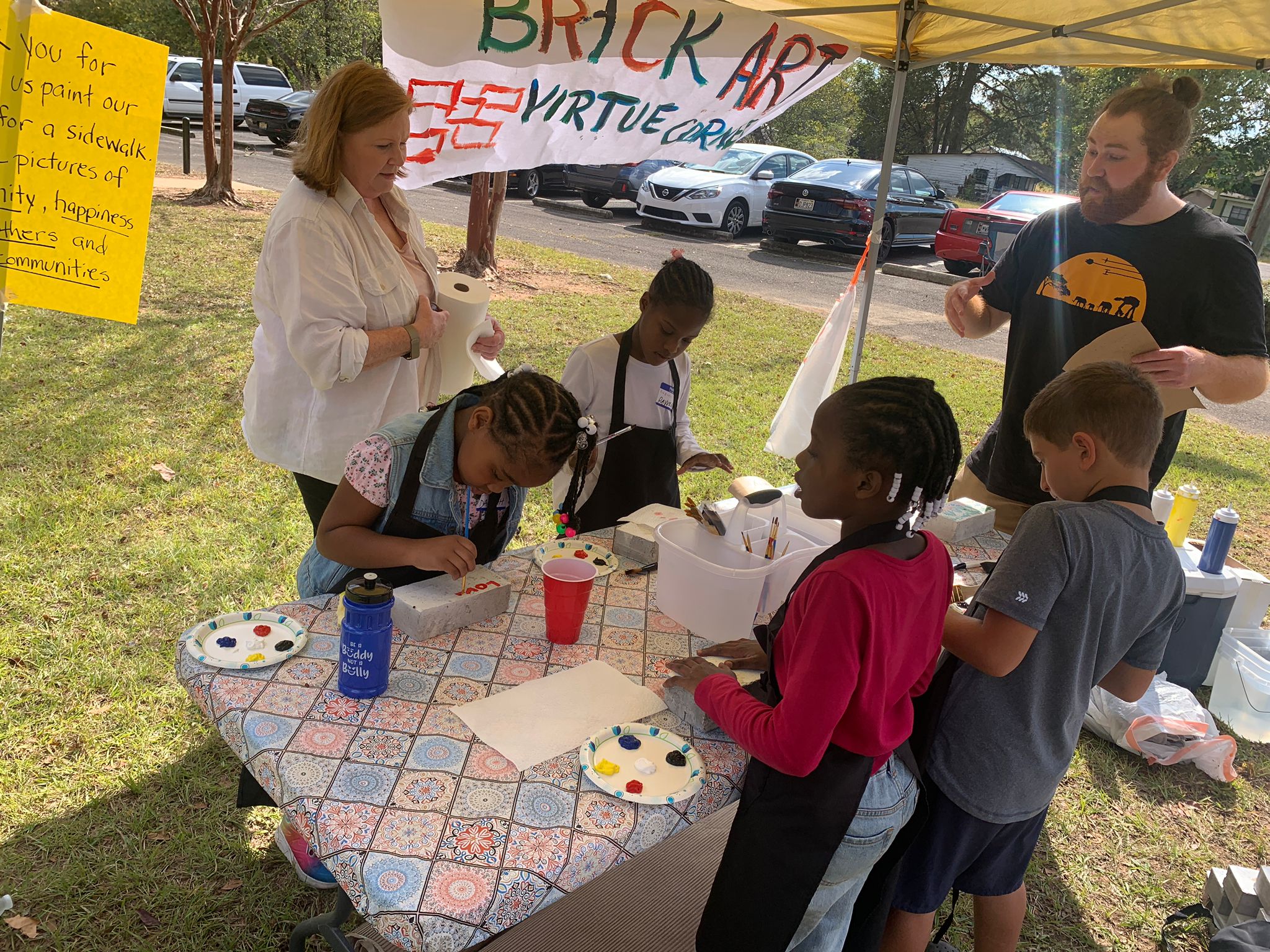 Several children paint messages on bricks with the guidance of two adults.