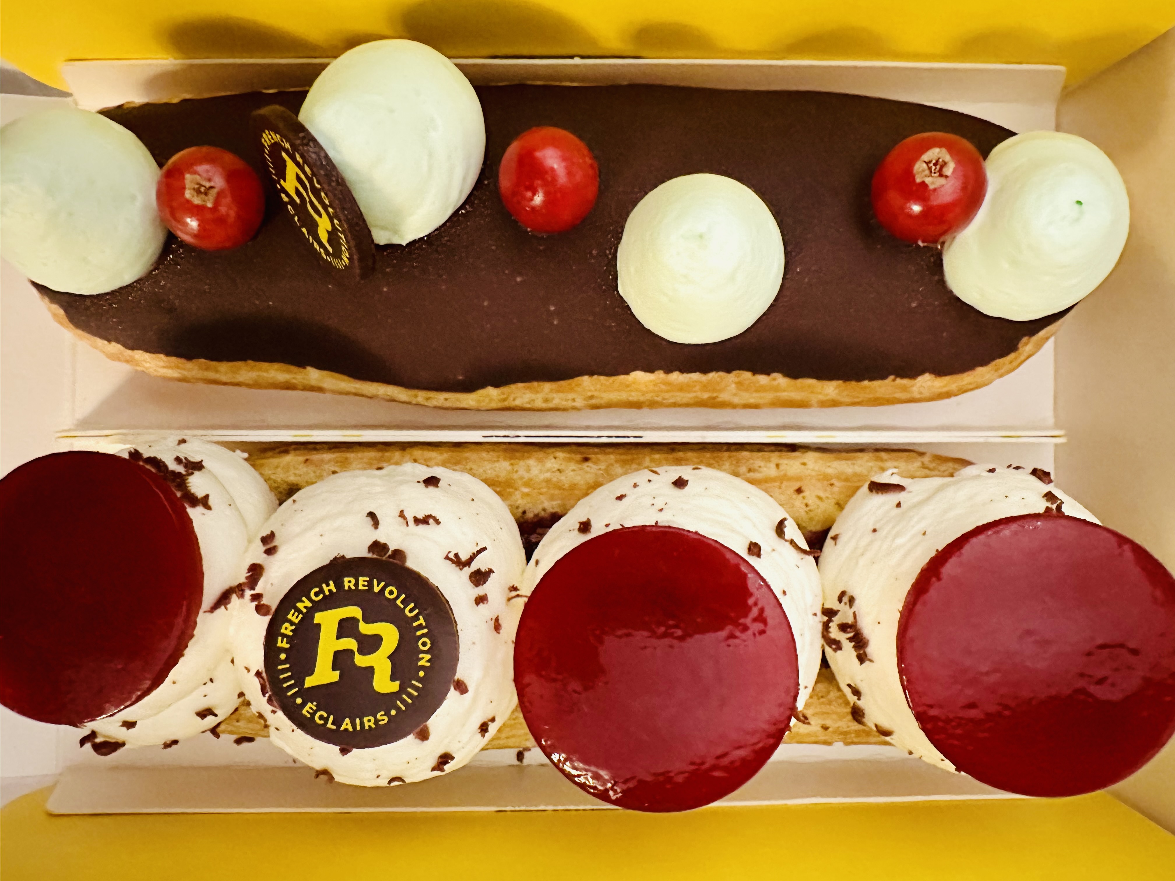 Two ornate eclairs are decorated with whipped cream, chocolate, and fruit.