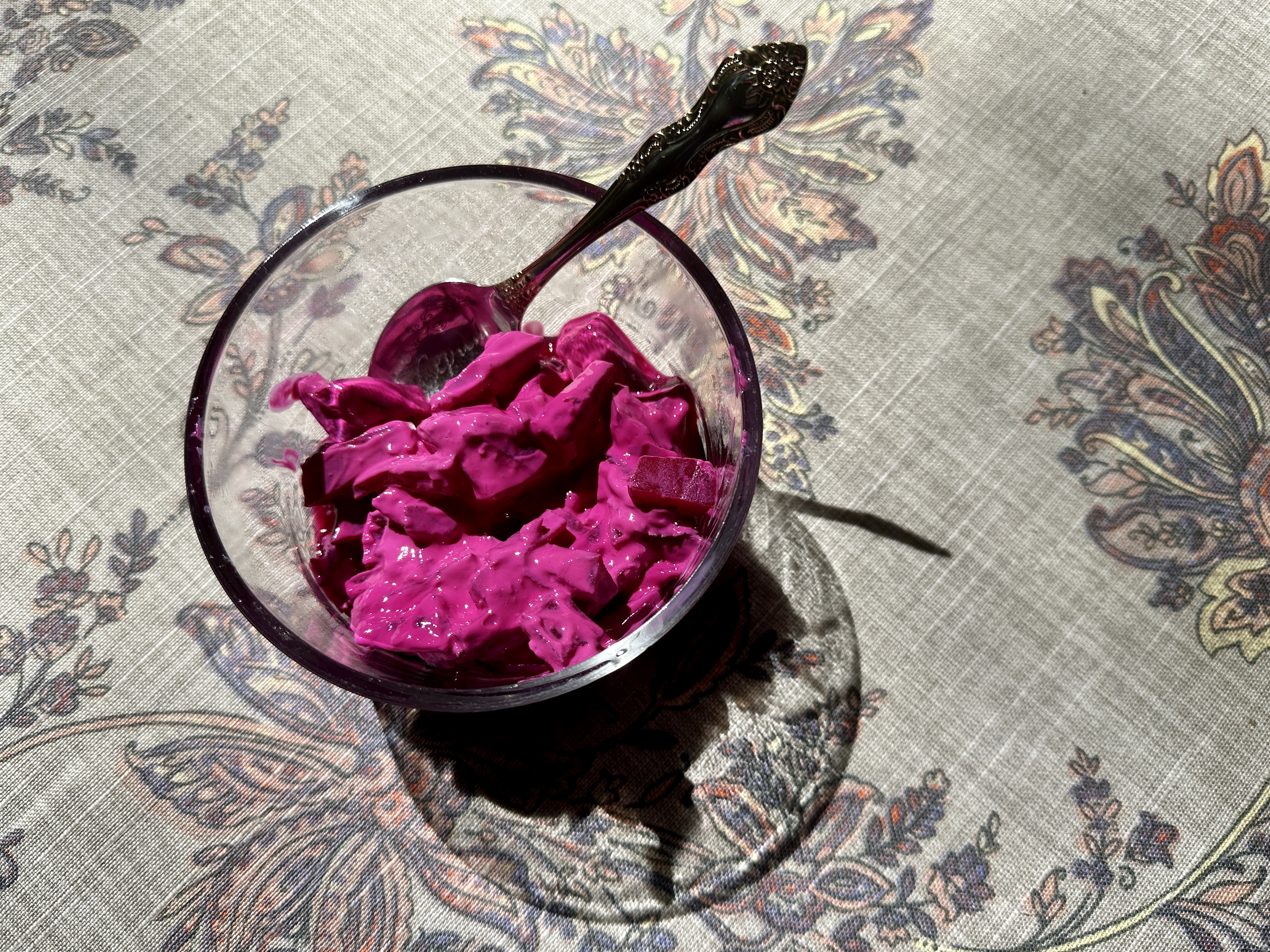 Bright pink beet salad in a glass bowl with a spoon.