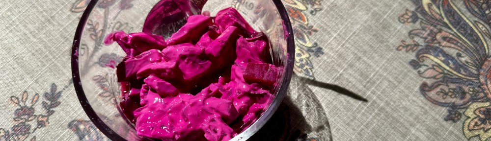Bright pink beet salad in a glass bowl with a spoon.