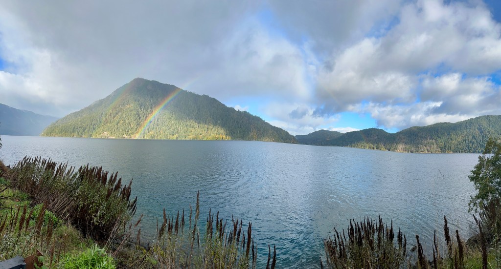 A rainbow arcs in front of a green mountain and above a large lake.