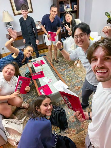 A group of young adults sitting in a circle smiles at the camera, holding up their Baha'i books.