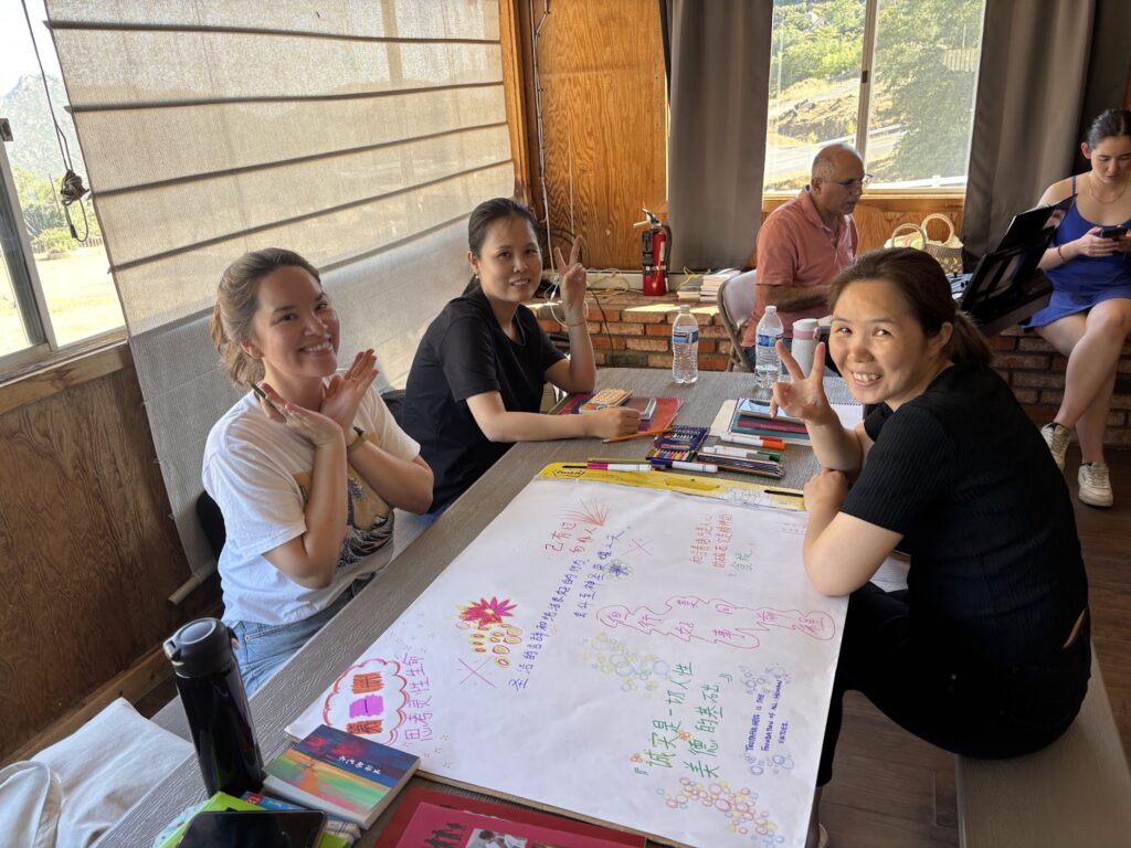 Several people sit around a table, where they are writing together on a large sheet of paper.