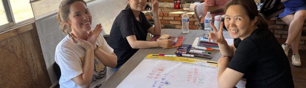 Several people sit around a table, where they are writing together on a large sheet of paper.