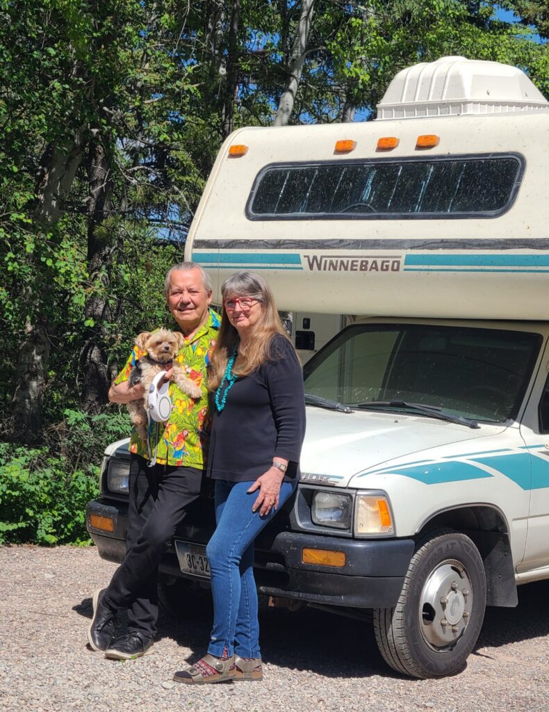 A man, woman, and dog pose in front of an RV camper.