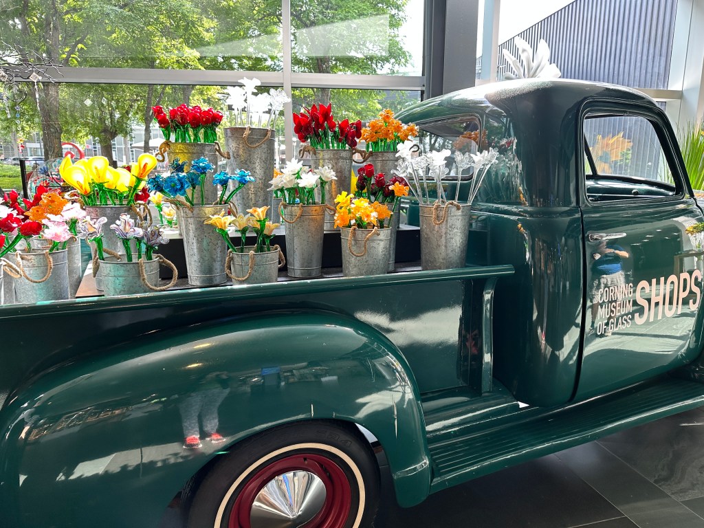 An old-fashioned pickup truck holds buckets of glass flowers.