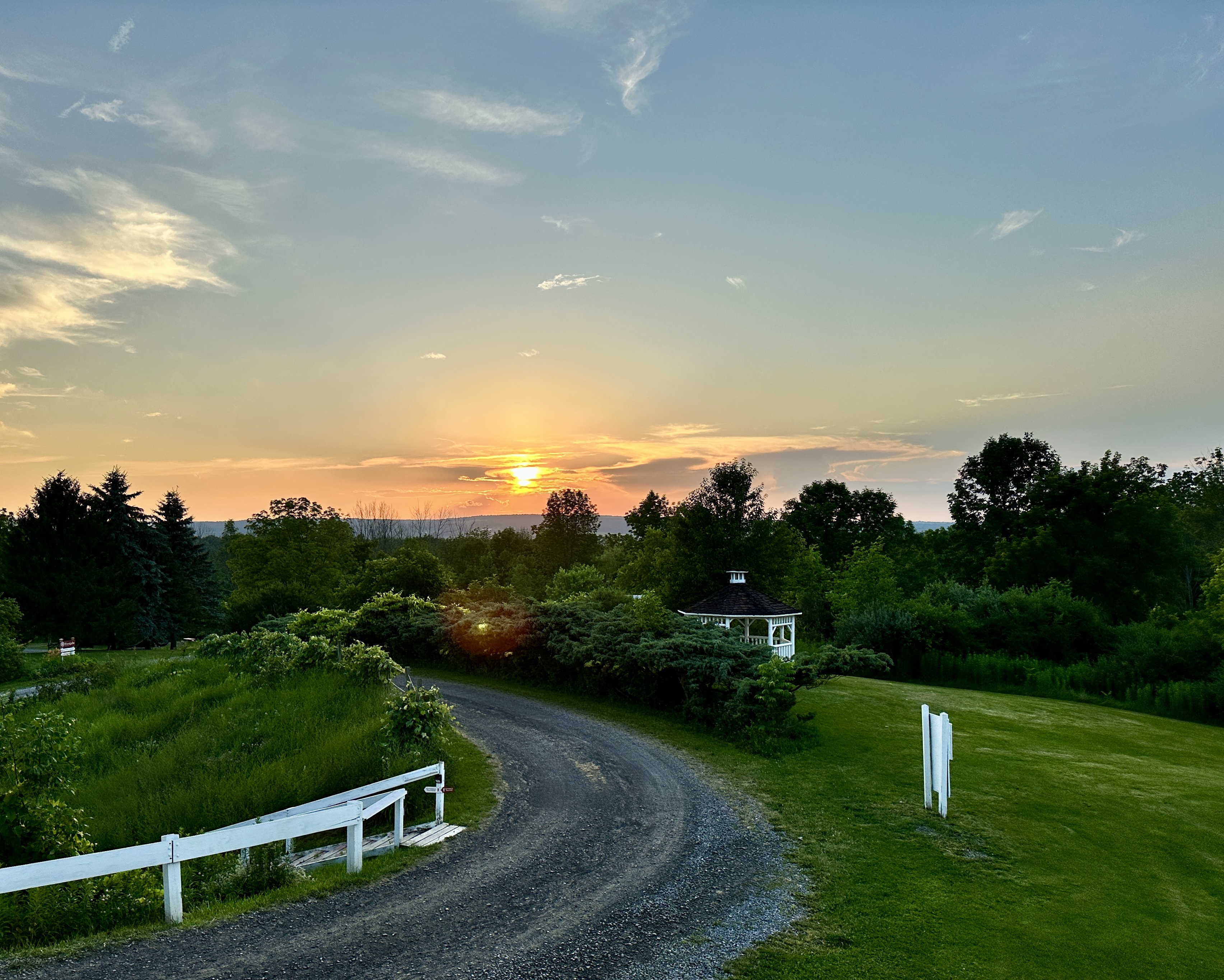 A gravel road and lawn at sunset, with a low mountain in the distance.